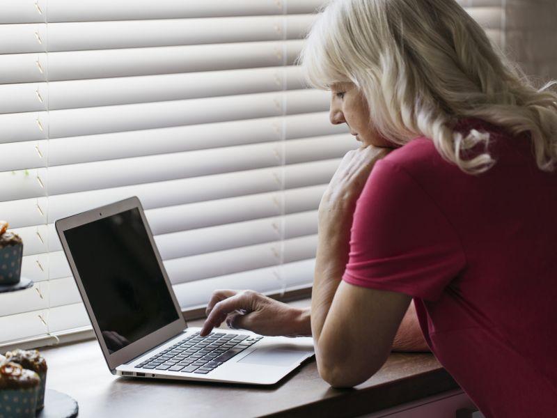 Mujer madura que usa la computadora portatil cerca de la ventana
