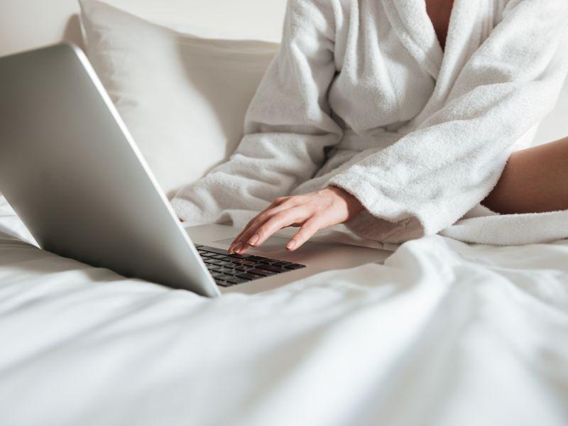 Mujer en bata de bano en la cama y usando laptop