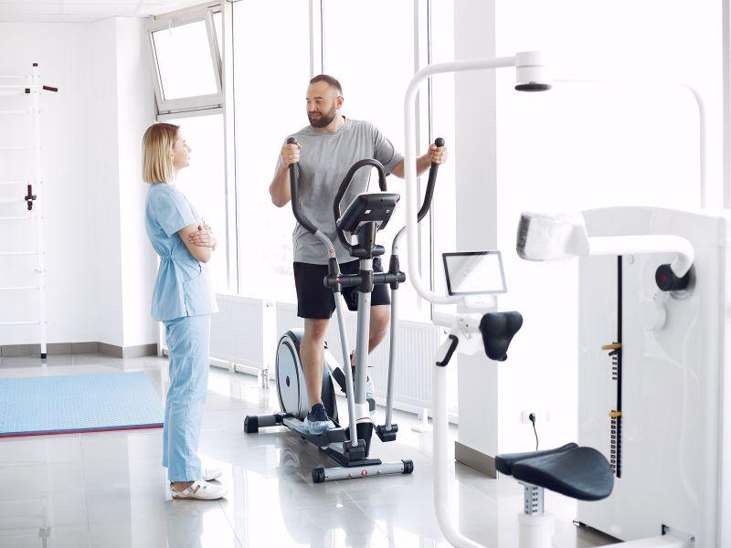 Paciente haciendo ejercicio en bicicleta de spinning en el gimnasio con el terapeuta