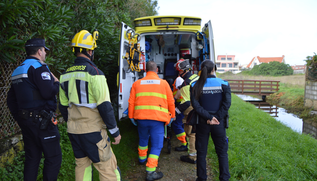 El personal técnico de emergencias sanitarias del 061 traslada en una ambulancia a un ciclista herido al caerse de la bicicleta en una pasarela de madera en Os Areiros, en Aguiño