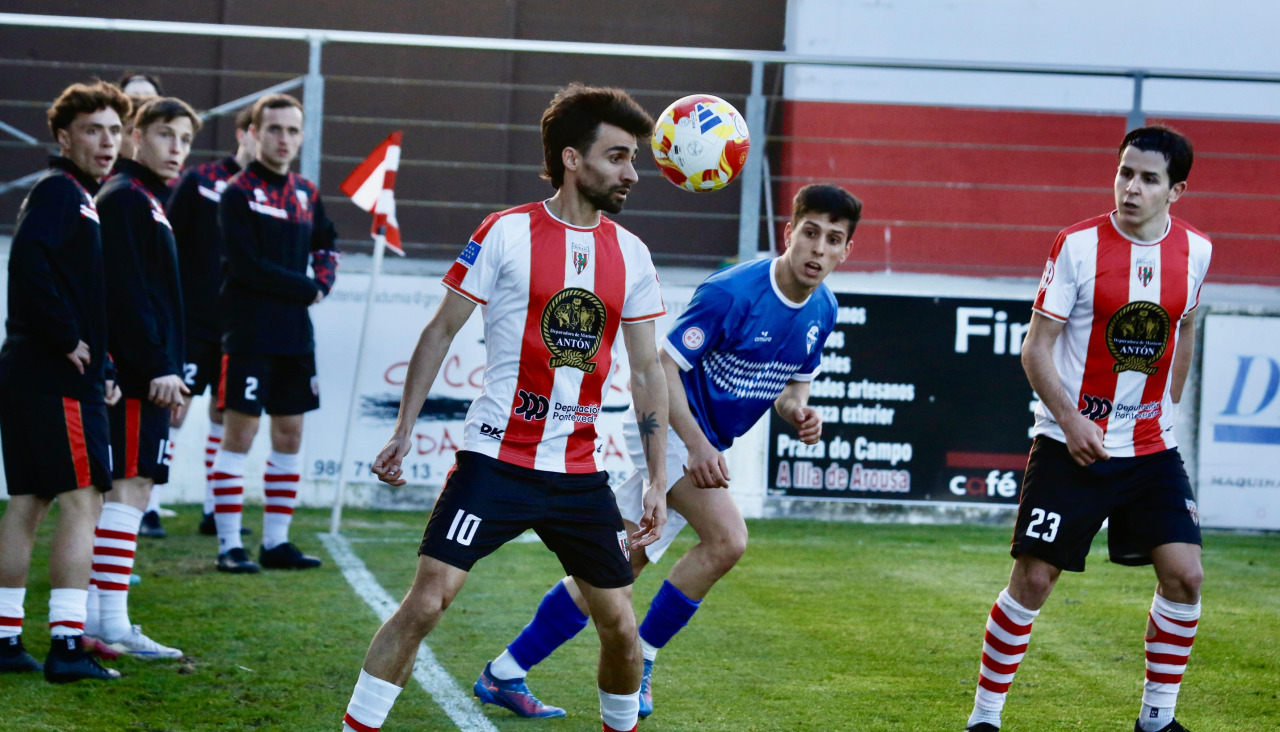 Julio Rey controla el balón ante la atenta mirada de los jugadores locales que calientan en la banda