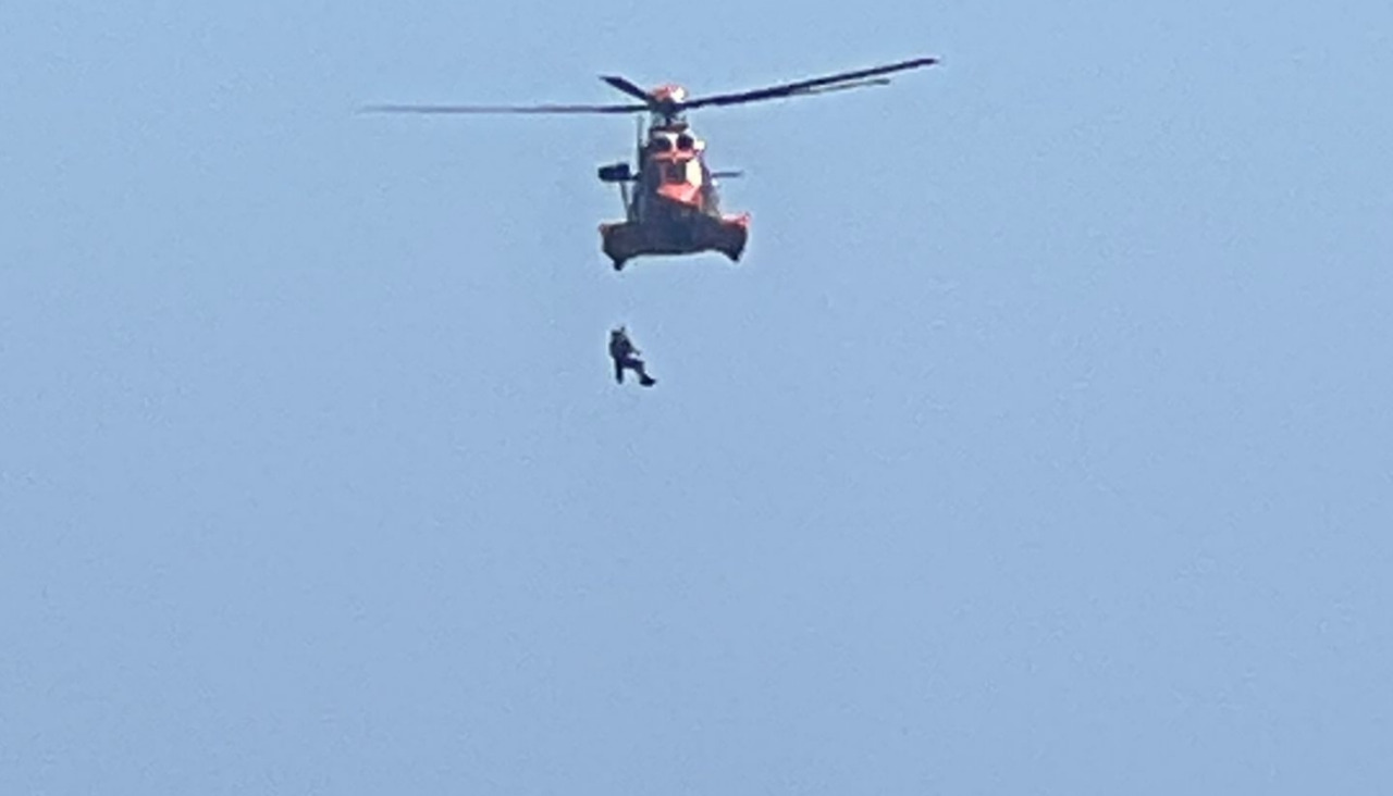 Un rescatador descendió de la aeronave pàra recoger a una persona que aguardaba en unas rocas conocidas como islote de A Perilla